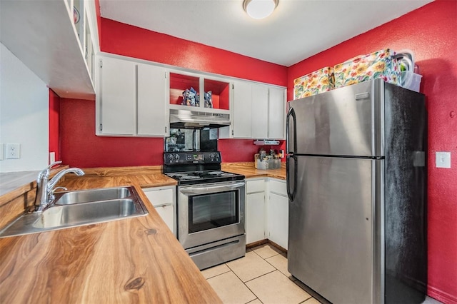 kitchen with wooden counters, stainless steel appliances, sink, light tile patterned floors, and white cabinets