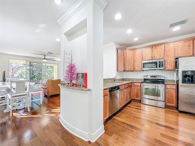 kitchen with ceiling fan, light stone counters, crown molding, appliances with stainless steel finishes, and hardwood / wood-style flooring