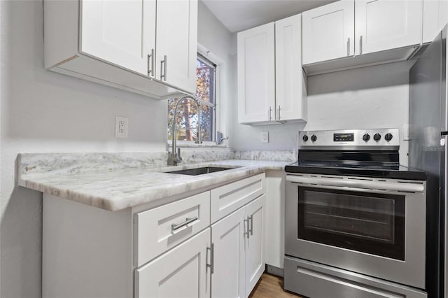 kitchen with sink, light hardwood / wood-style flooring, light stone countertops, appliances with stainless steel finishes, and white cabinetry