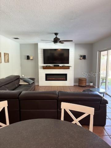 tiled living room with a textured ceiling, a large fireplace, and ceiling fan