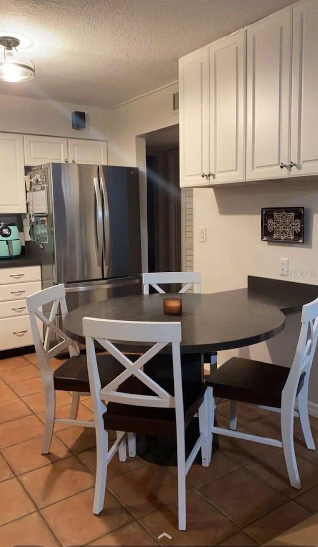 kitchen featuring white cabinets, tile patterned flooring, a textured ceiling, and stainless steel refrigerator