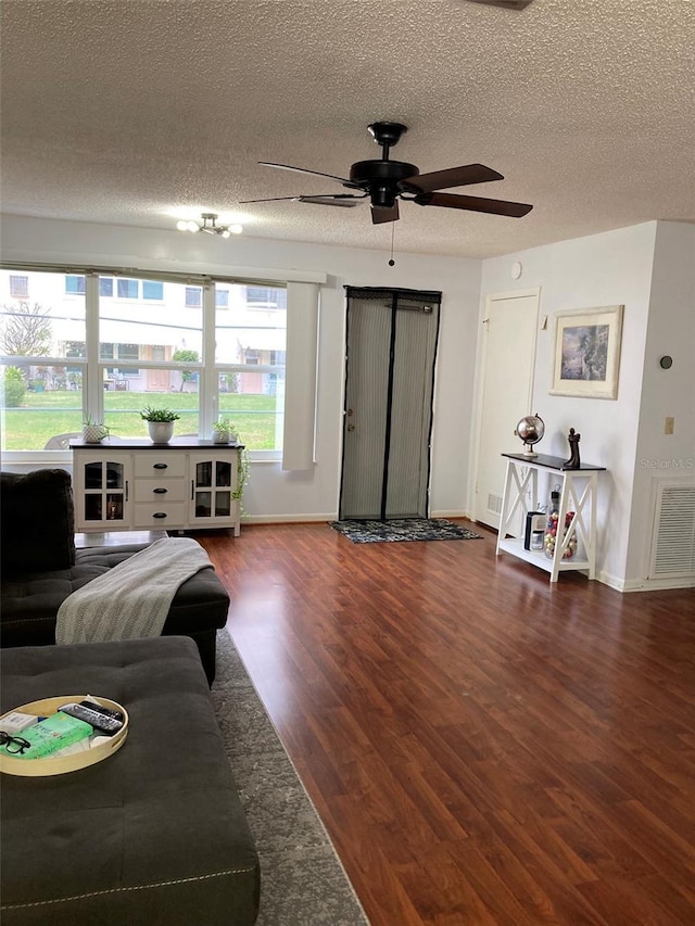 living room with dark wood-type flooring, ceiling fan, and a textured ceiling