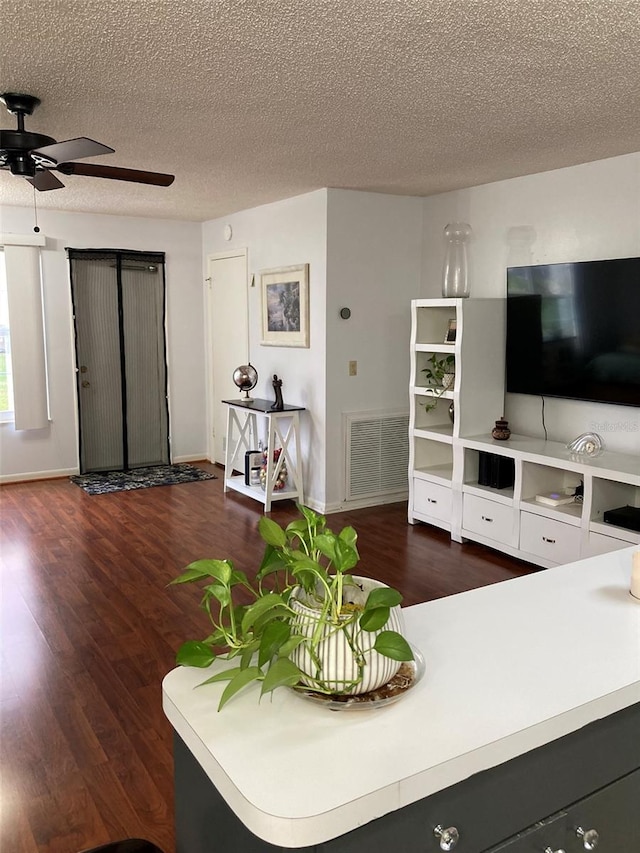 living room featuring dark hardwood / wood-style flooring, ceiling fan, and a textured ceiling