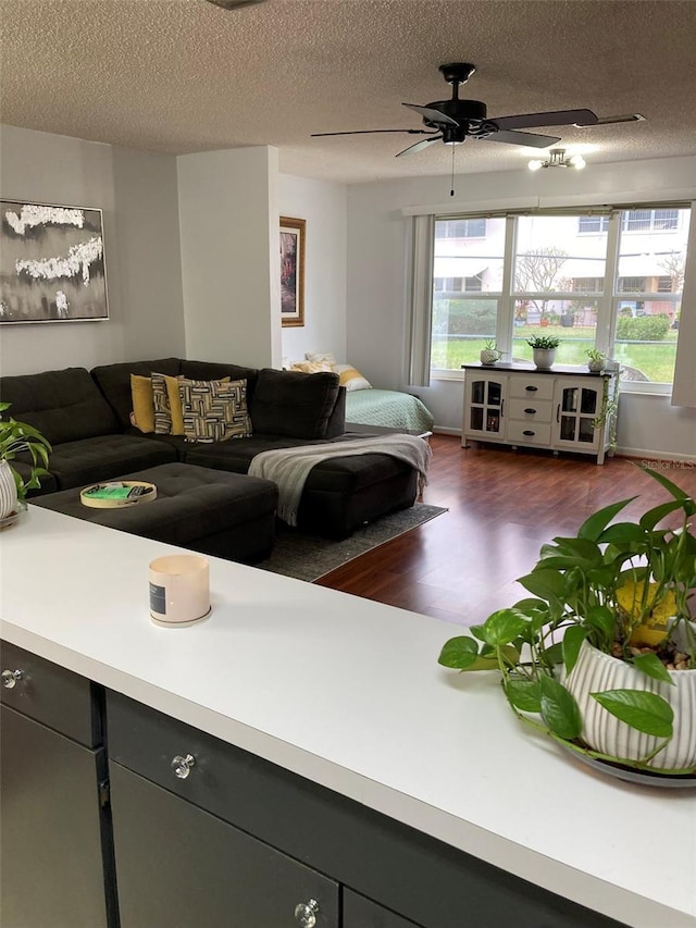 living room featuring dark wood-type flooring, ceiling fan, a textured ceiling, and a wealth of natural light