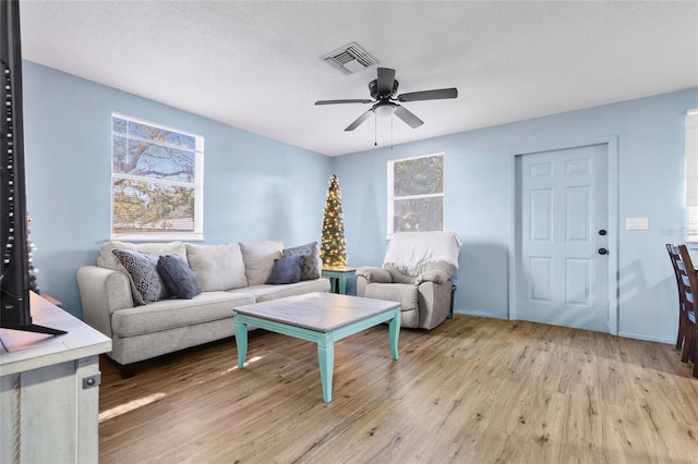 living room with ceiling fan, light hardwood / wood-style flooring, a healthy amount of sunlight, and a textured ceiling