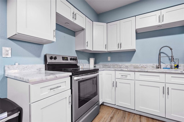 kitchen featuring light stone countertops, light wood-type flooring, sink, electric stove, and white cabinetry