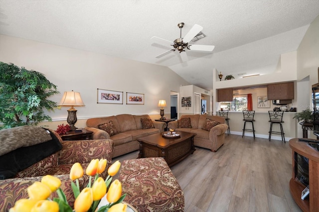 living room featuring ceiling fan, light wood-type flooring, lofted ceiling, and a textured ceiling