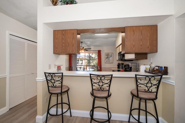 kitchen featuring a kitchen breakfast bar, kitchen peninsula, ceiling fan, a textured ceiling, and wood-type flooring