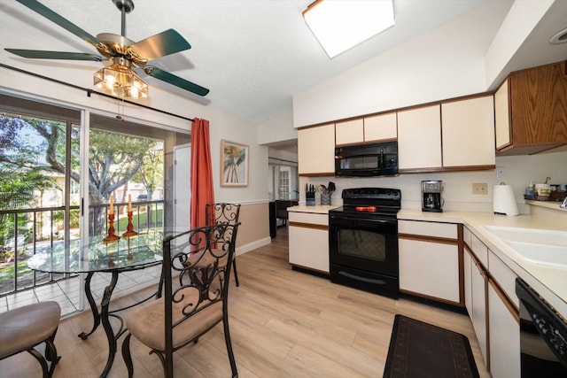 kitchen with light wood-type flooring, ceiling fan, sink, black appliances, and lofted ceiling