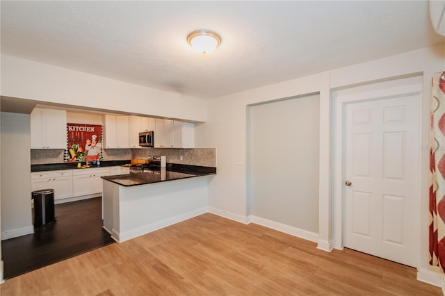 kitchen featuring tasteful backsplash, kitchen peninsula, appliances with stainless steel finishes, white cabinets, and hardwood / wood-style flooring