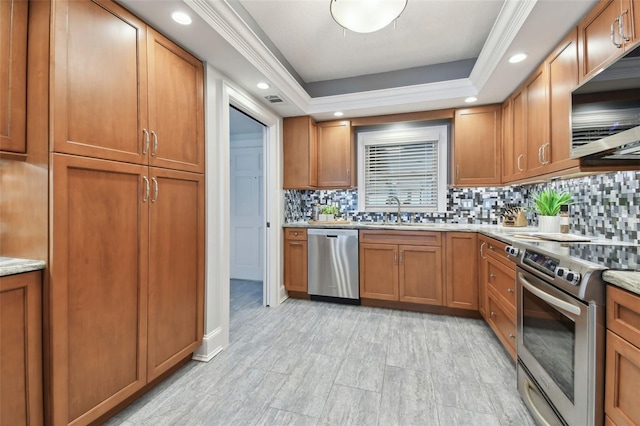 kitchen with a raised ceiling, sink, decorative backsplash, appliances with stainless steel finishes, and light stone counters