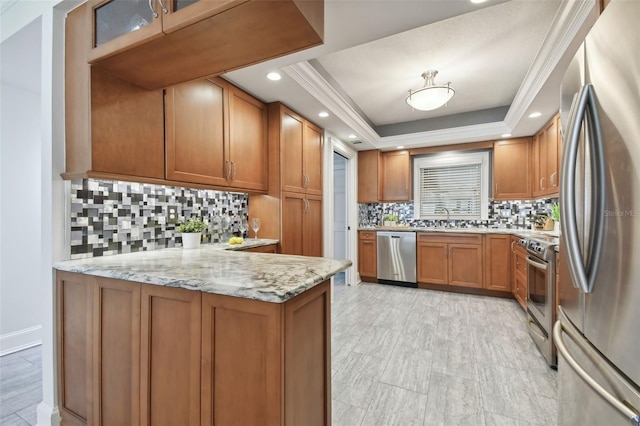 kitchen with a raised ceiling, sink, appliances with stainless steel finishes, light stone counters, and kitchen peninsula