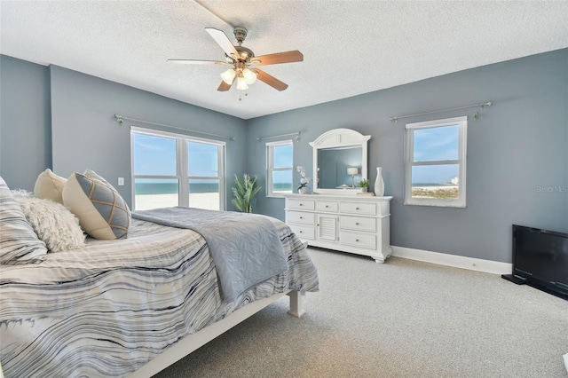 bedroom featuring a textured ceiling, a water view, ceiling fan, and light colored carpet