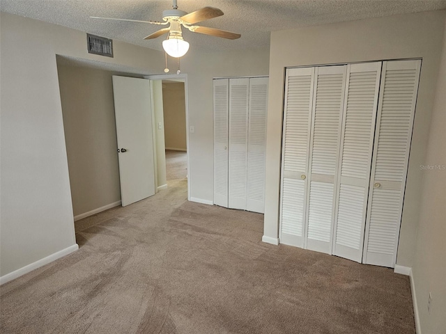 unfurnished bedroom with multiple closets, ceiling fan, light colored carpet, and a textured ceiling