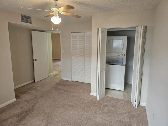 unfurnished bedroom with a textured ceiling, light carpet, ceiling fan, and stacked washer and clothes dryer