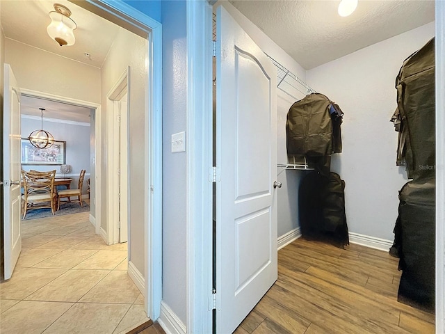 hall with a textured ceiling, light hardwood / wood-style flooring, a notable chandelier, and crown molding