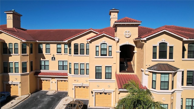 view of front of house featuring an attached garage, a tile roof, a chimney, and stucco siding