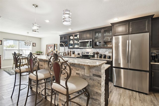 kitchen featuring a center island with sink, appliances with stainless steel finishes, decorative light fixtures, light hardwood / wood-style floors, and dark brown cabinets