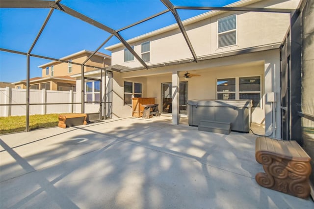 rear view of house featuring glass enclosure, ceiling fan, a patio, and a hot tub