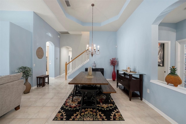 dining space with a raised ceiling, light tile patterned floors, and an inviting chandelier