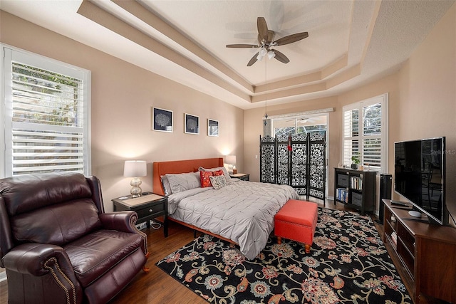 bedroom featuring multiple windows, dark hardwood / wood-style floors, ceiling fan, and a tray ceiling