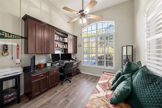 home office with ceiling fan, vaulted ceiling, built in desk, and light hardwood / wood-style flooring