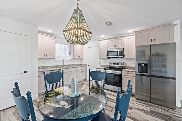 kitchen featuring sink, hanging light fixtures, a notable chandelier, appliances with stainless steel finishes, and light wood-type flooring