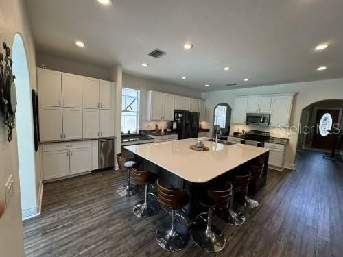 kitchen featuring dark wood-type flooring, an island with sink, a kitchen bar, white cabinets, and appliances with stainless steel finishes