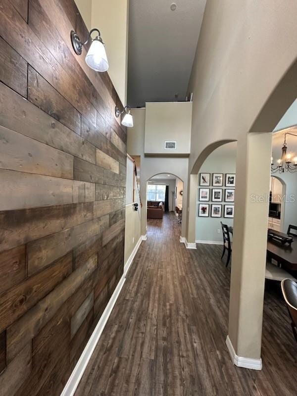 hall featuring wooden walls, high vaulted ceiling, dark wood-type flooring, and a notable chandelier