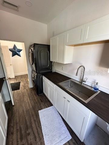 kitchen with stacked washer and dryer, white cabinetry, dark wood-type flooring, and sink