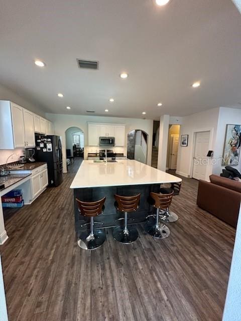 kitchen with a kitchen breakfast bar, dark hardwood / wood-style flooring, black refrigerator, and a center island with sink