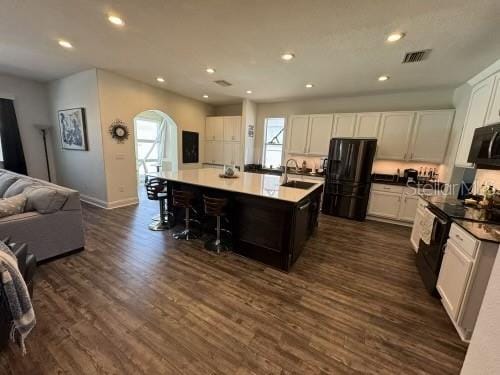 kitchen featuring black appliances, white cabinets, an island with sink, and a wealth of natural light