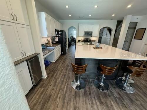 kitchen with dark hardwood / wood-style flooring, an island with sink, a kitchen bar, white cabinets, and appliances with stainless steel finishes