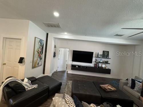 living room with a textured ceiling, dark hardwood / wood-style flooring, and ceiling fan