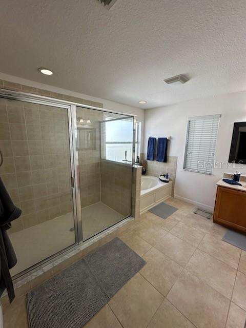 bathroom with plus walk in shower, vanity, a textured ceiling, and tile patterned floors