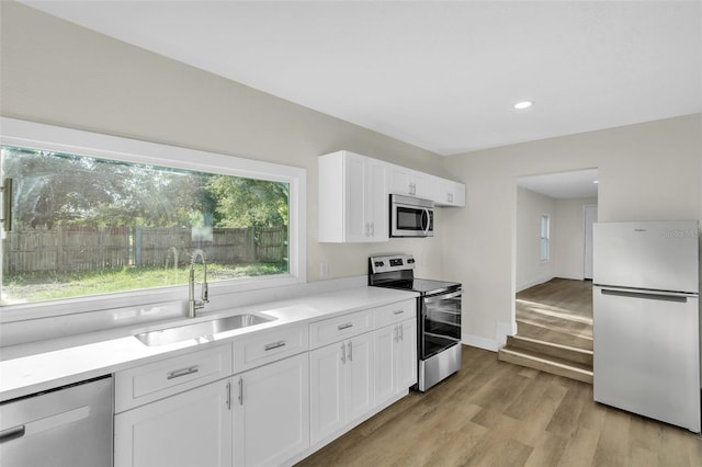 kitchen with sink, white cabinets, stainless steel appliances, and light hardwood / wood-style flooring