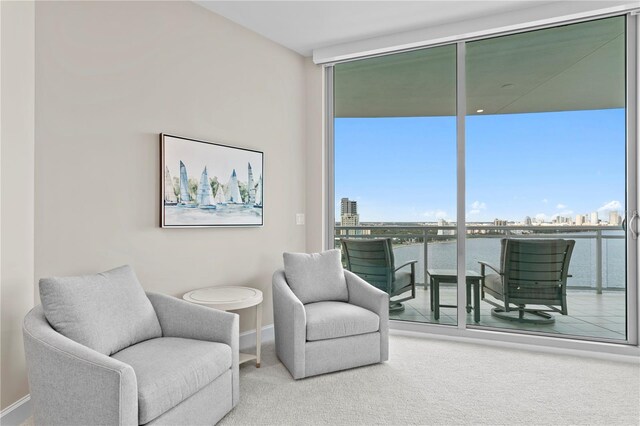 living area with expansive windows, a water view, and carpet floors