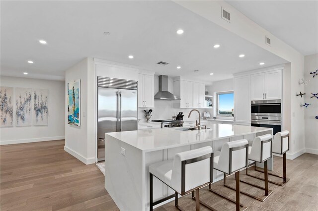 kitchen featuring sink, wall chimney exhaust hood, stainless steel appliances, and a center island with sink