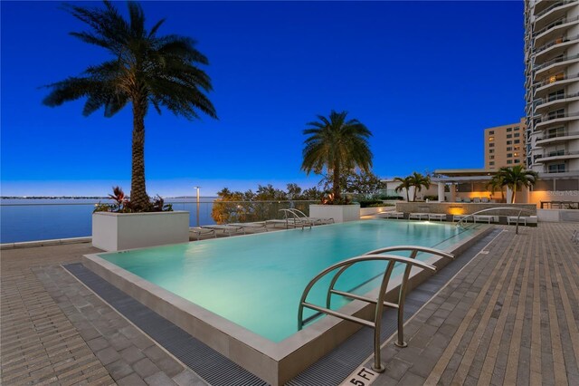 pool at dusk with a water view and a patio area