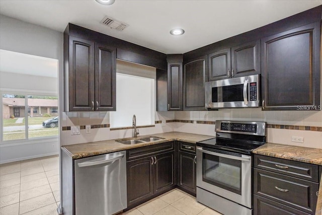 kitchen featuring dark brown cabinetry, sink, decorative backsplash, light tile patterned flooring, and appliances with stainless steel finishes