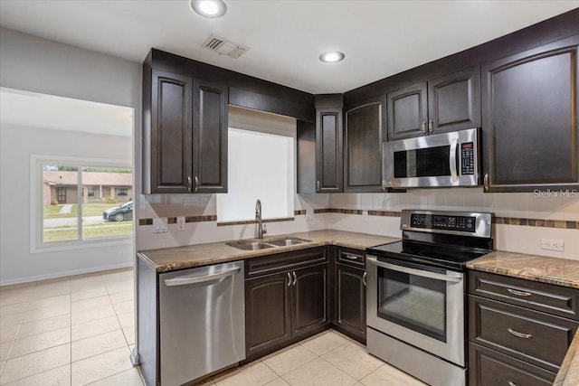 kitchen with appliances with stainless steel finishes, tasteful backsplash, dark brown cabinetry, sink, and light tile patterned flooring