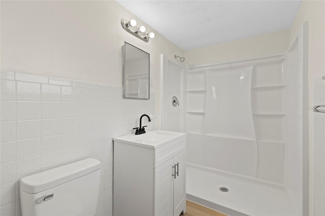 bathroom with vanity, a shower, toilet, a textured ceiling, and tile walls