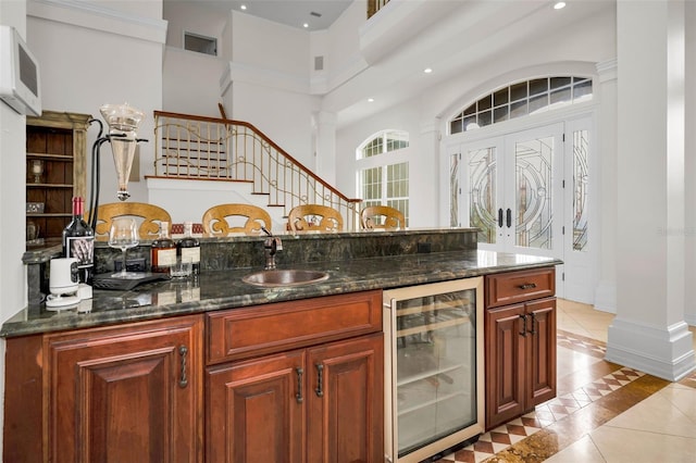 119 8th St E, Tierra Verde, FL 33715 - bar area featuring wine cooler, inlaid floor details, light tile patterned flooring, stairway, and a towering ceiling
