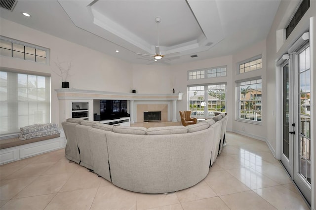 tiled living room with ceiling fan and a tray ceiling