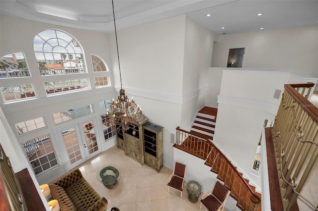 tiled living room with an inviting chandelier, crown molding, a high ceiling, and french doors