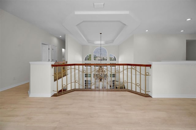 hallway with a raised ceiling, light wood-type flooring, and an inviting chandelier