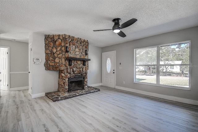 unfurnished living room featuring ceiling fan, light hardwood / wood-style floors, a stone fireplace, and a textured ceiling