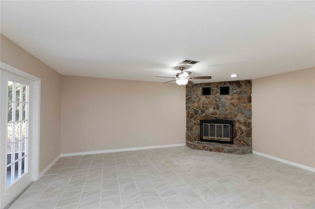 unfurnished living room with a textured ceiling, a stone fireplace, and ceiling fan