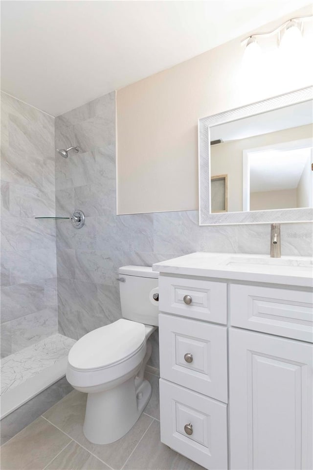 bathroom with vanity, tiled shower, tile walls, tile patterned flooring, and toilet