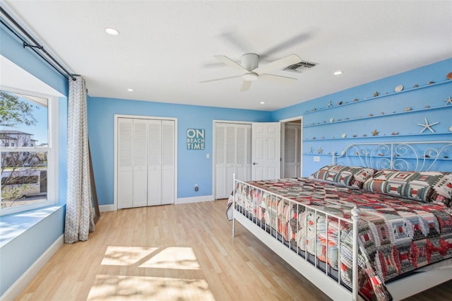 bedroom featuring two closets, light hardwood / wood-style floors, and ceiling fan